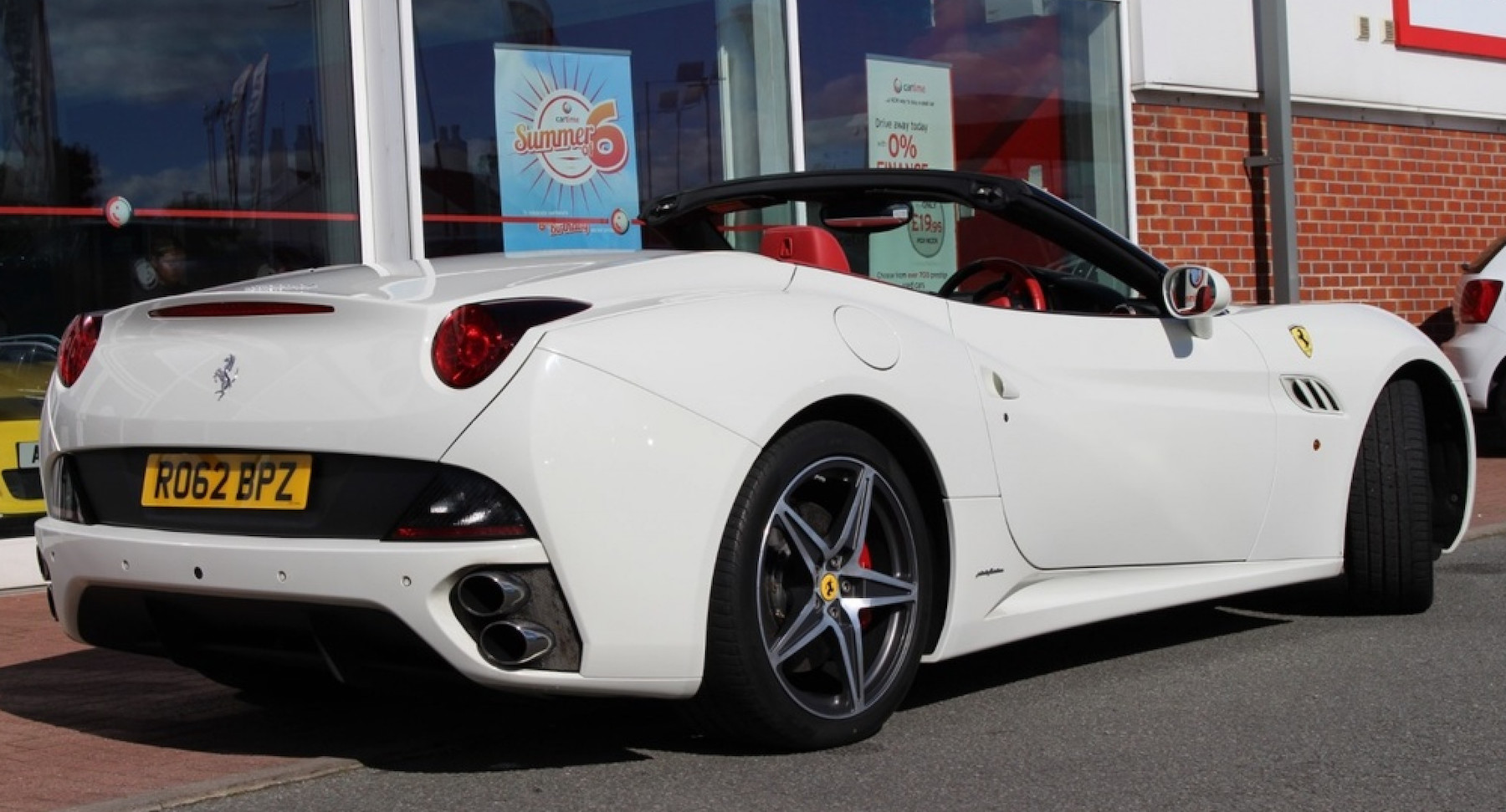 Rear or white Ferrari California parked facing right in front of cartime showroom